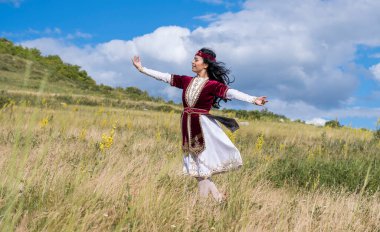 Güzel kırmızı takım elbiseli genç parlak bir kız mavi bir yaz gökyüzüne karşı ulusal bir dans yapıyor.