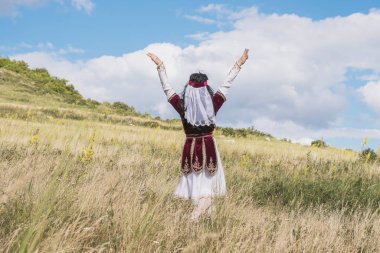 Güzel kırmızı takım elbiseli genç parlak bir kız mavi bir yaz gökyüzüne karşı ulusal bir dans yapıyor.