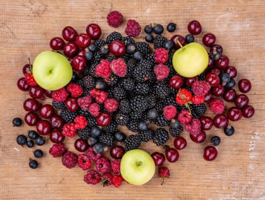 Olgun böğürtlen böğürtlen, kırmızı kiraz, ahududu, siyah frenk üzümü ve elmalar ahşap bir masada yatıyor.