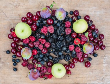 Olgun böğürtlen böğürtlen, kırmızı kiraz, ahududu, siyah frenk üzümü, elma ve erik ağaçları ahşap bir masada uzanır.