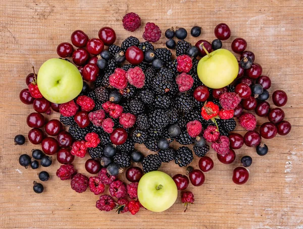 Olgun böğürtlen böğürtlen, kırmızı kiraz, ahududu, siyah frenk üzümü ve elmalar ahşap bir masada yatıyor.