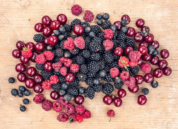 Olgun böğürtlen böğürtlen, kırmızı kiraz, ahududu ve siyah frenk üzümü ahşap bir masada yatar.
