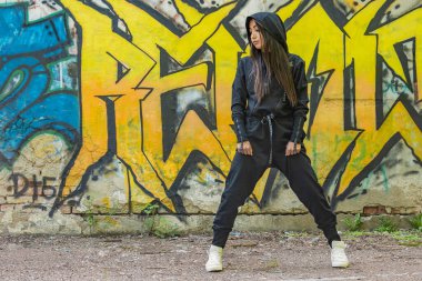 Tarz sahibi siyah tulumlu genç bir kız duvarın arka planında grafiti desenli fiziksel egzersizlere hazırlanıyor.