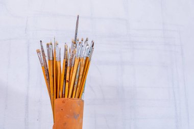 Resim yapmak için bir dizi ince fırça beyaz bir tuvalin arka planında duran bir tüpte durur.