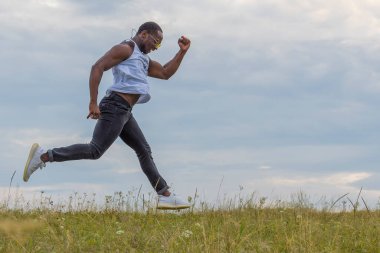 Genç ve güçlü bir atlet, mavi bir yaz gökyüzüne değmeden yeşil bir alanda koşar..