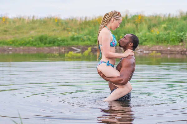 Young couple bathes in the lake. A strong guy lifted the girl in his arms and tries to kiss