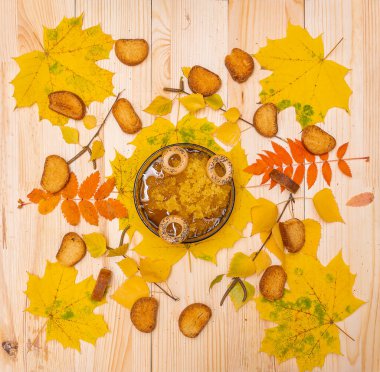 Bashkir bal ve kurutuculu bir fincan, sarı yapraklar ve ekmek kırıntılarıyla çevrili ahşap bir masanın üzerinde duruyor. Tatlı bir sonbahar ikramı.