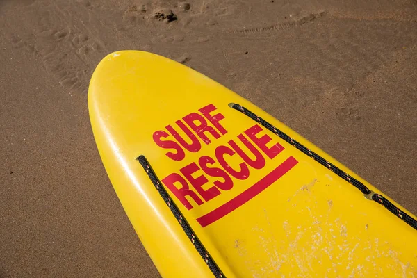 Lifeguard yellow board with surf rescue on the wet sand