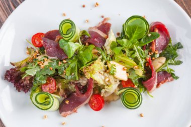 Salad with duck and vegetables on white plate