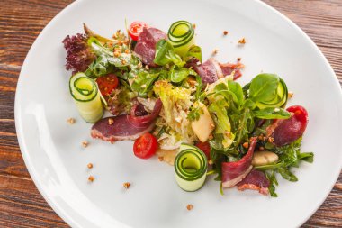 Salad with duck and vegetables on white plate