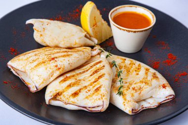 Soslu ızgara kalamar ve siyah tabakta limon.