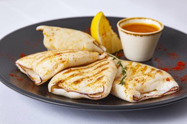 Soslu ızgara kalamar ve siyah tabakta limon.