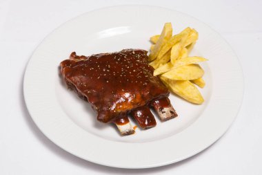 Soslu ızgara domuz kaburgası, patates kızartması, beyaz tabakta baharat.