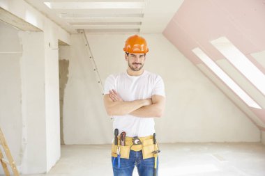 Kask ve alet kemeri duran inşaat alanında giymiş yakışıklı genç tamirci. 