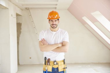 Kask ve alet kemeri duran inşaat alanında giymiş yakışıklı genç tamirci. 
