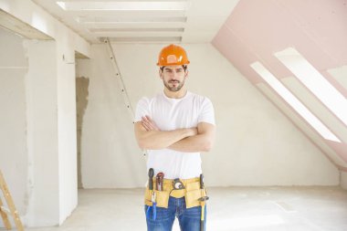 Kask ve alet kemeri duran inşaat alanında giymiş yakışıklı genç tamirci. 