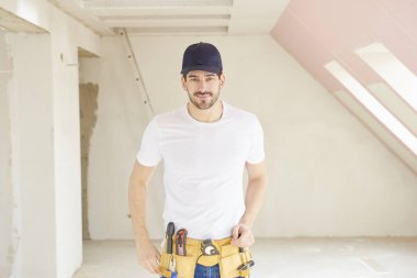 Genç tamirci inşaat alanında duran beyzbol kap ve aracı kemer takmaya portresi.