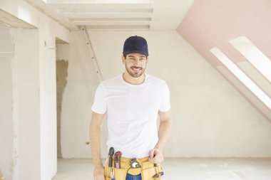 Genç tamirci inşaat alanında duran beyzbol kap ve aracı kemer takmaya portresi.