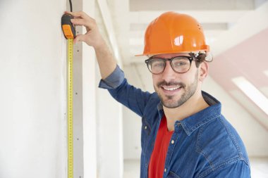 İnşaatta çalışırken zor nefret giyen ve ölçüm bandı Smling genç inşaat işçisi.