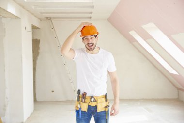 Kask ve alet kemeri duran inşaat alanında giymiş yakışıklı genç tamirci. 