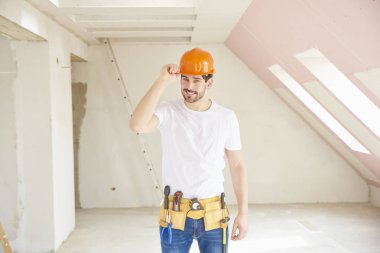 Kask ve alet kemeri duran inşaat alanında giymiş yakışıklı genç tamirci.  