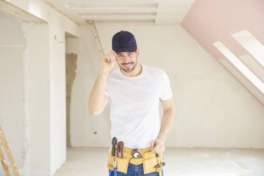 İnşaat alanında dururken şapka ve aracı kemer takmaya yakışıklı genç tamirci.  