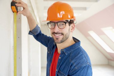 İnşaatta çalışırken zor nefret giyen ve ölçüm bandı Smling genç inşaat işçisi.