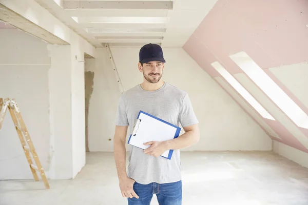 Young renovation worker holding clipboard in his hand while standing at constrcution site.