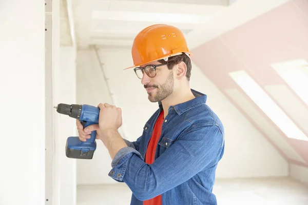 年轻修理工戴安全帽和工具带的肖像在工地施工时使用锤钻驱动程序 — 图库照片