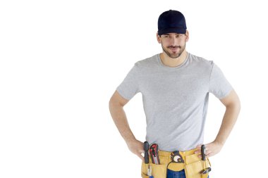 Portrait of handsome young handyman wearing baseball cap and tool belt while standing at isolated white background with copy space. clipart
