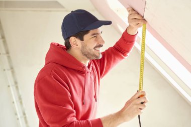 İnşaat alanında çalışırken mezura kullanan genç adamın portresi. 