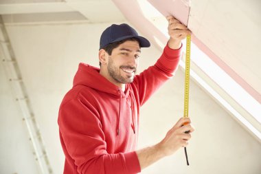 İnşaat alanında çalışırken mezura kullanan genç adamın portresi. 