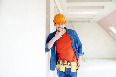 Yakışıklı genç tamirci evde kask ve alet kemeri dururken giyen portresi.