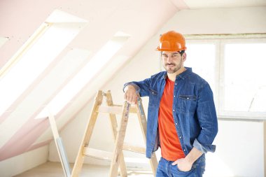 Merdiven yanında dururken baret inşaat alanındaki giyen genç tamirci portresi. 