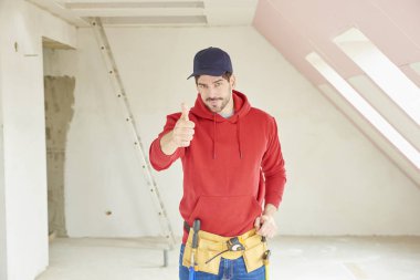 İnşaat alanında ayakta ve thums pes etmek başarılı genç tamirci portresi.