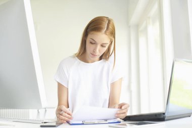 Dizüstü bilgisayar ve bilgisayar başında modern ofis önünde oturma sırasında bazı evrak işlerini yaparken Genç satış asistanı işkadını portresi. 