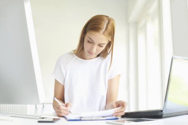 Dizüstü bilgisayar ve bilgisayar başında modern ofis önünde oturma sırasında bazı evrak işlerini yaparken Genç satış asistanı işkadını portresi. 