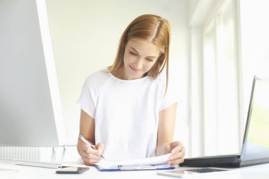 Dizüstü bilgisayar ve bilgisayar başında modern ofis önünde oturma sırasında bazı evrak işlerini yaparken Genç satış asistanı işkadını portresi. 