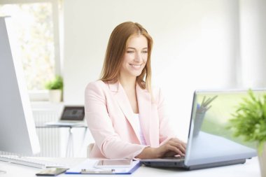 Modern ofiste oturan ve dizüstü bilgisayarda çalışma güzel genç iş kadını portresi. 