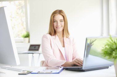 Yakın çekim modern ofis oturma ve dizüstü bilgisayarda çalışma güzel genç gülümseyen mali Yardımcısı işkadını portresi. 