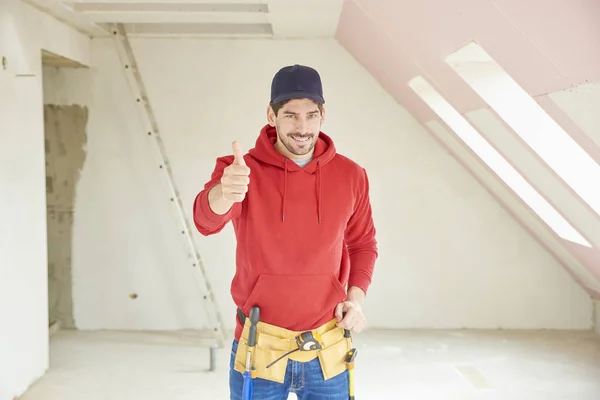 Portrait of handsome young handyman giving thumbs up while standing at construction area at the the house.