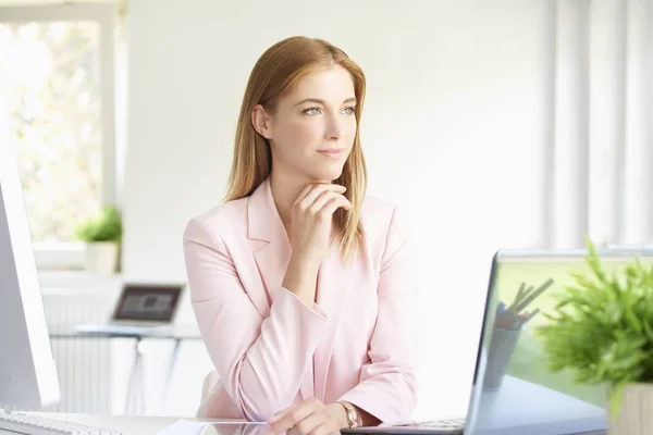 年轻漂亮的女实业家坐在现代办公室的肖像 并期待在笔记本电脑时若有所思 — 图库照片