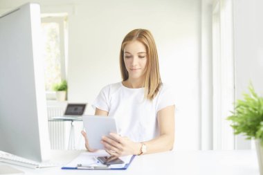 Genç çekici satış kadın ofis masası oturma ve yeni proje üzerinde çalışma sırasında dijital tablet kullanma. 