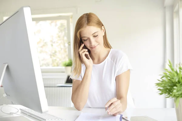 漂亮的年轻销售助理女商人打电话和做一些文书工作 而坐在电脑前 在一个现代化的办公室 — 图库照片