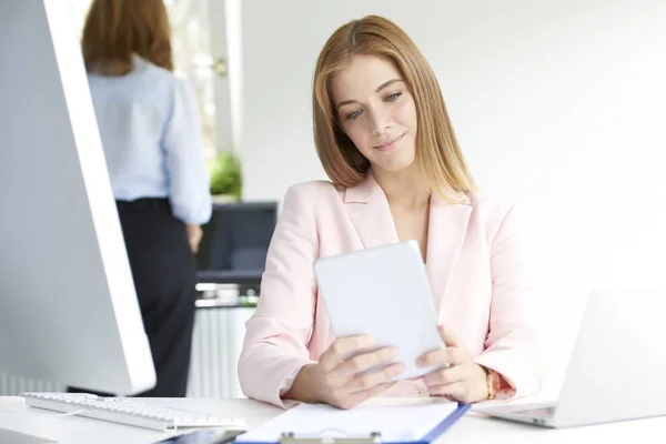 魅力的な若い実業家彼女の手でデジタル タブレットを保持して オフィスの机に座っていると作業しながらインターネット上で閲覧 — ストック写真