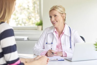 Bilgisayar ve dizüstü bilgisayar kullanıyorsanız ve tanı ile çalışıyorsanız gülümseyen yaşlı kadın doktor