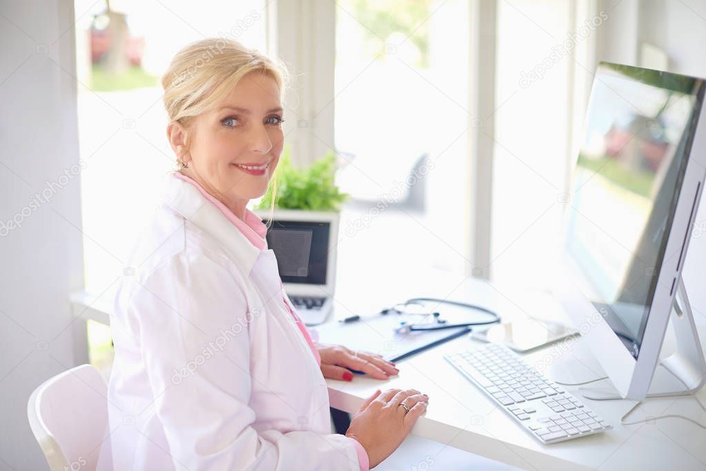 Smiling senior female doctor working in light office