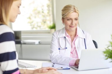 Bir kadın doktor hastasını ile doktor ofisinde otururken dizüstü kullanarak atış. 