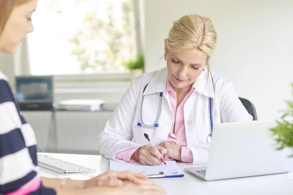 Shot of female doctor talking to woman and writing medical report at the doctor\'s room.