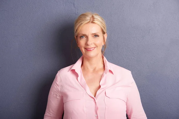 Cropped shot of beautiful mature woman looking at camera and smiling while standing at grey wall.